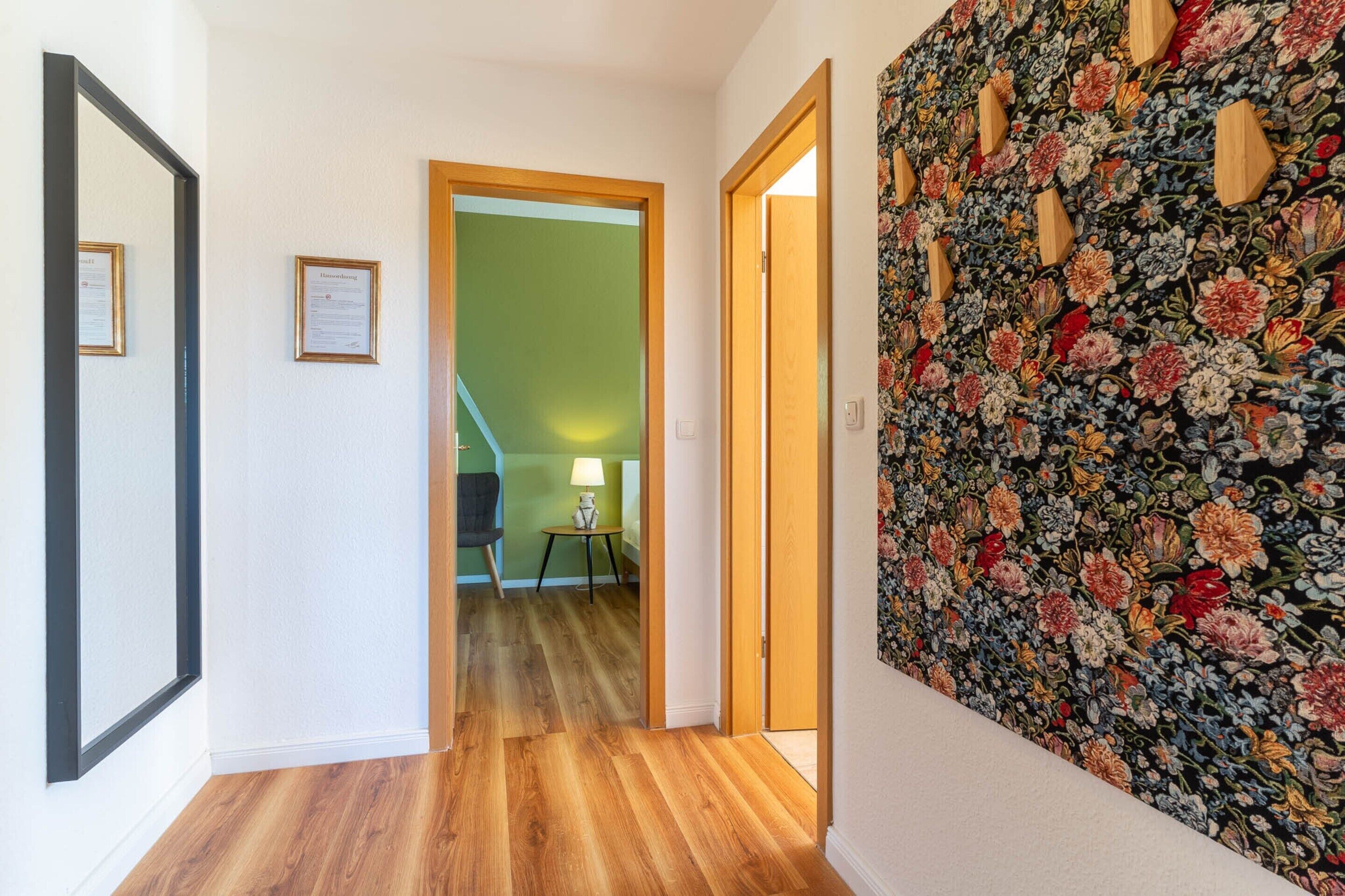 Un couloir doté d’un plancher en bois, d’un mur vert et d’un autre mur orné d’un motif floral.