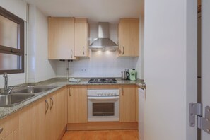 A compact kitchen with wooden cabinets, a stainless steel sink, a gas stove, and a built-in oven. - Seafront Apt Torre Valentina (Calonge)