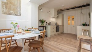 A modern kitchen with white cabinetry, a wooden dining table with chairs, and a small island with a plant.