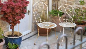 A stone building with a white door, two white metal chairs, and potted plants.