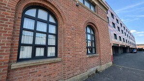 Un bâtiment en briques rouges, doté de grandes fenêtres en arc de cercle et d’un parking situé devant.