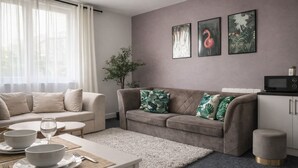 Un salon moderne avec un canapé beige, une table à manger avec de l’assiette et des couverts, et un coin cuisine équipé d’un four à micro-ondes.