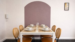 Un coin repas avec une table blanche dressée pour quatre personnes, entourée de chaises en osier.