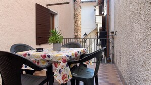 Eine Terrasse mit Tisch und Stühlen, einem Blumentopf und einer Wand mit Fenster und Rollo.
