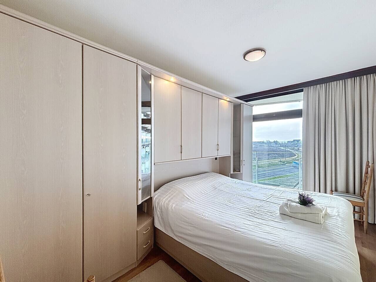 A hotel room with a large bed, a wardrobe, and a view of a cityscape.