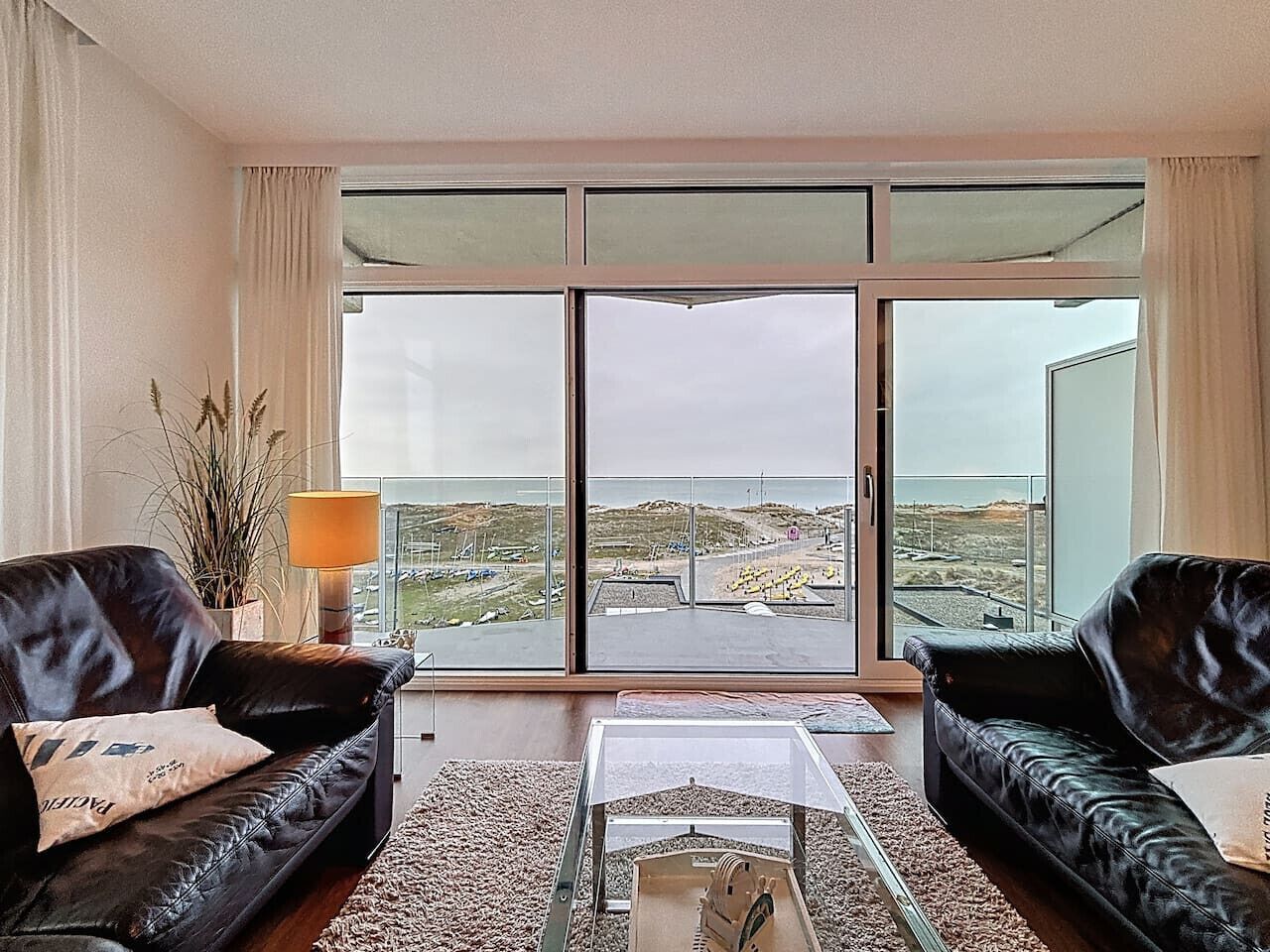 Una sala de estar moderna con dos sofás de cuero negro, una mesa de centro de vidrio y vistas a un paisaje costero a través de amplios ventanales.