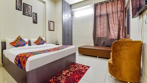 Une chambre d’hôtel avec un lit, un canapé, une chaise, un tapis rouge à motifs et des œuvres d’art accrochées au mur.