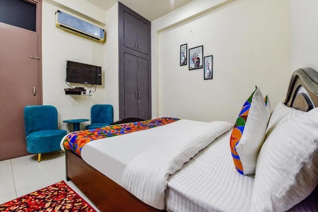 Une chambre d’hôtel avec un lit, deux chaises bleues, une petite table, un téléviseur et une armoire.