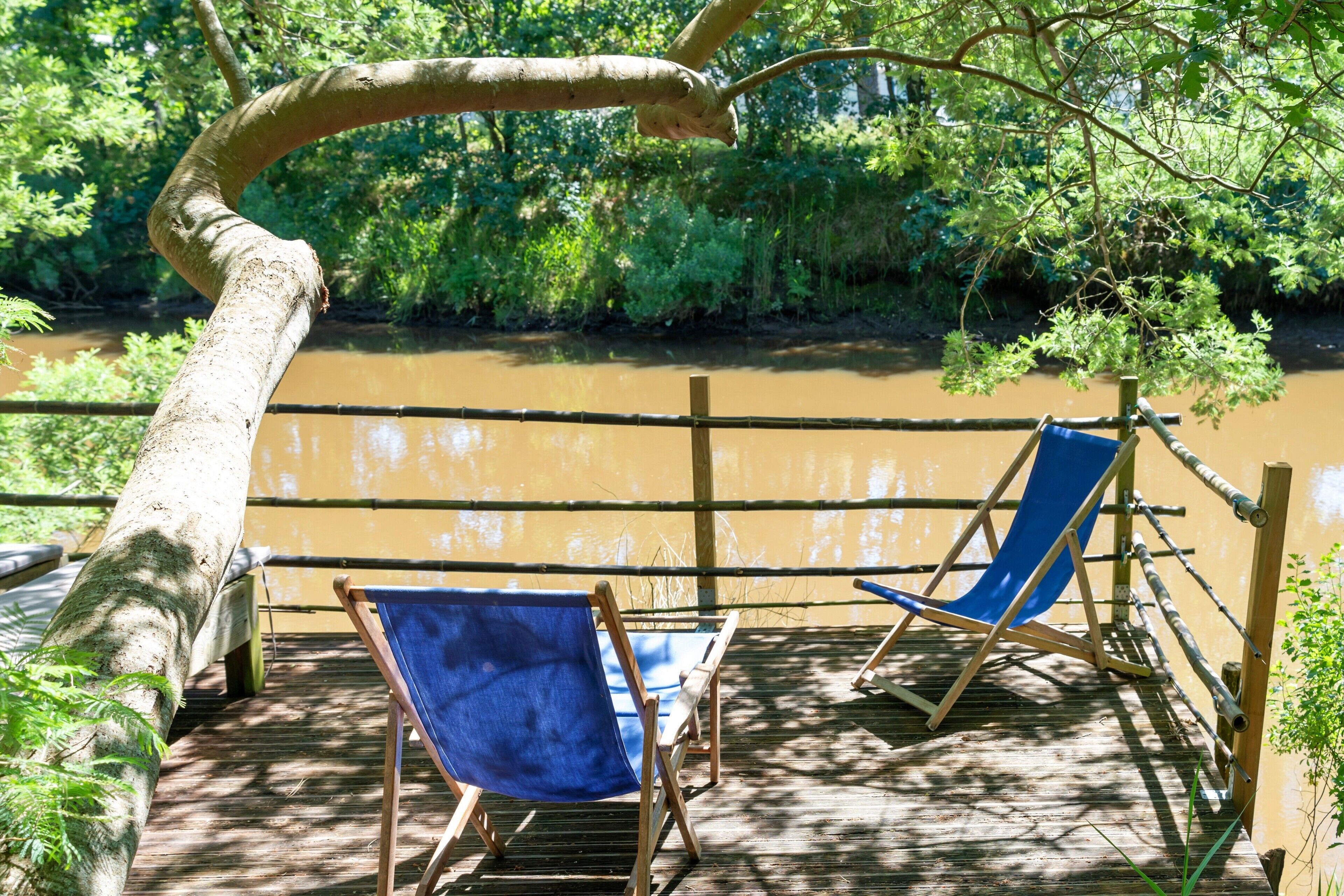 A wooden deck with two blue chairs and a wooden railing overlooking a river.