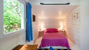 Ein Schlafzimmer mit einem Bett, zwei Nachttischen mit Lampen, einem Fenster mit Vorhängen und Blick ins Grüne.