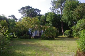 A grassy area with trees and a building with a bench. - Holiday Home “Villa Ananda - Kerala Annex” (Capbreton)