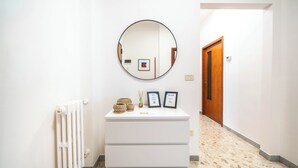 Een gang met een witte radiator, een ronde spiegel, een witte dressoir met drie lades en een bord met een welkomstboodschap.