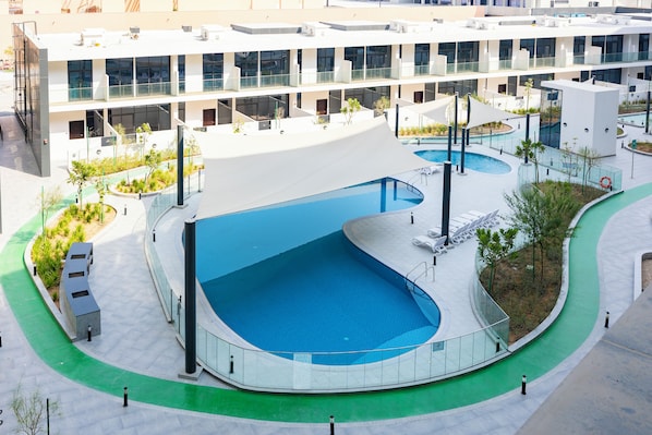 A modern building with a swimming pool, outdoor seating, and a landscaped area. - Bloomfields Studio in The Gate-Masdar (Abu Dhabi)