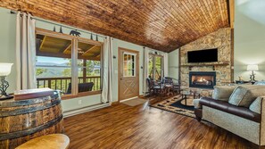 A cozy living room with a stone fireplace, wooden ceiling, and a view of the outdoors. - Scenic Serenity | Maggie Valley, 4BR, 3 BA, VIEWS! (Maggie Valley)