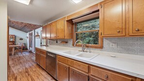 A kitchen with wooden cabinets, a white countertop, and a window with a view of greenery. - Scenic Serenity | Maggie Valley, 4BR, 3 BA, VIEWS! (Maggie Valley)