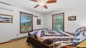 Una camera da letto con un letto, una ventola a soffitto e due finestre con persiane.