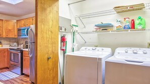 A compact kitchen with wooden cabinets, a stainless steel refrigerator, a microwave, a stove, and a washing machine. - Scenic Serenity | Maggie Valley, 4BR, 3 BA, VIEWS! (Maggie Valley)