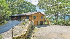 A wooden cabin with a stone foundation, a driveway, and a wooden staircase leading to the garage. - Scenic Serenity | Maggie Valley, 4BR, 3 BA, VIEWS! (Maggie Valley)