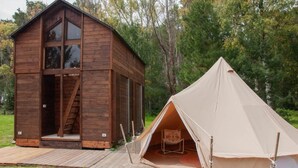 Une cabane en bois dotée d’une grande fenêtre et une tente installée à proximité.