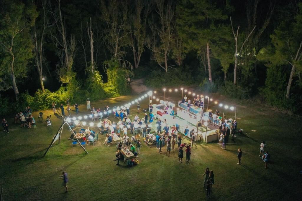 An outdoor event with a circular arrangement of tables and chairs, surrounded by trees.
