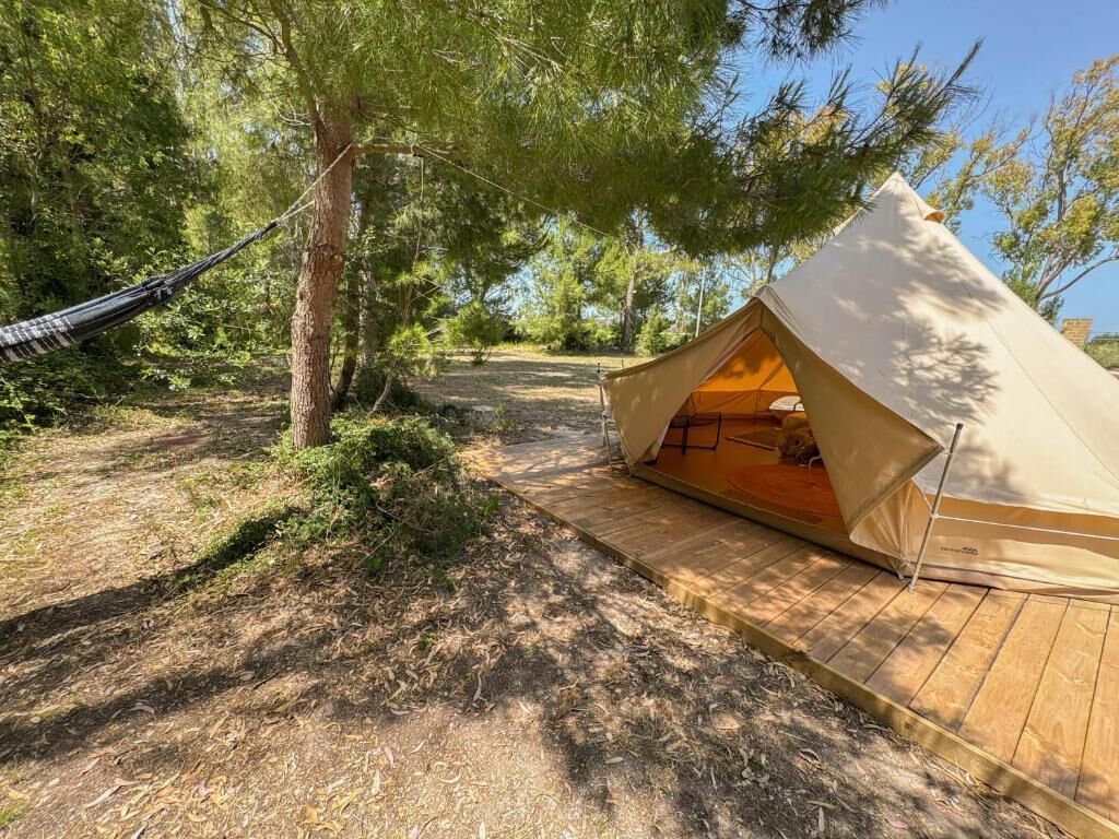 A tent with a wooden deck, surrounded by trees and a hammock.