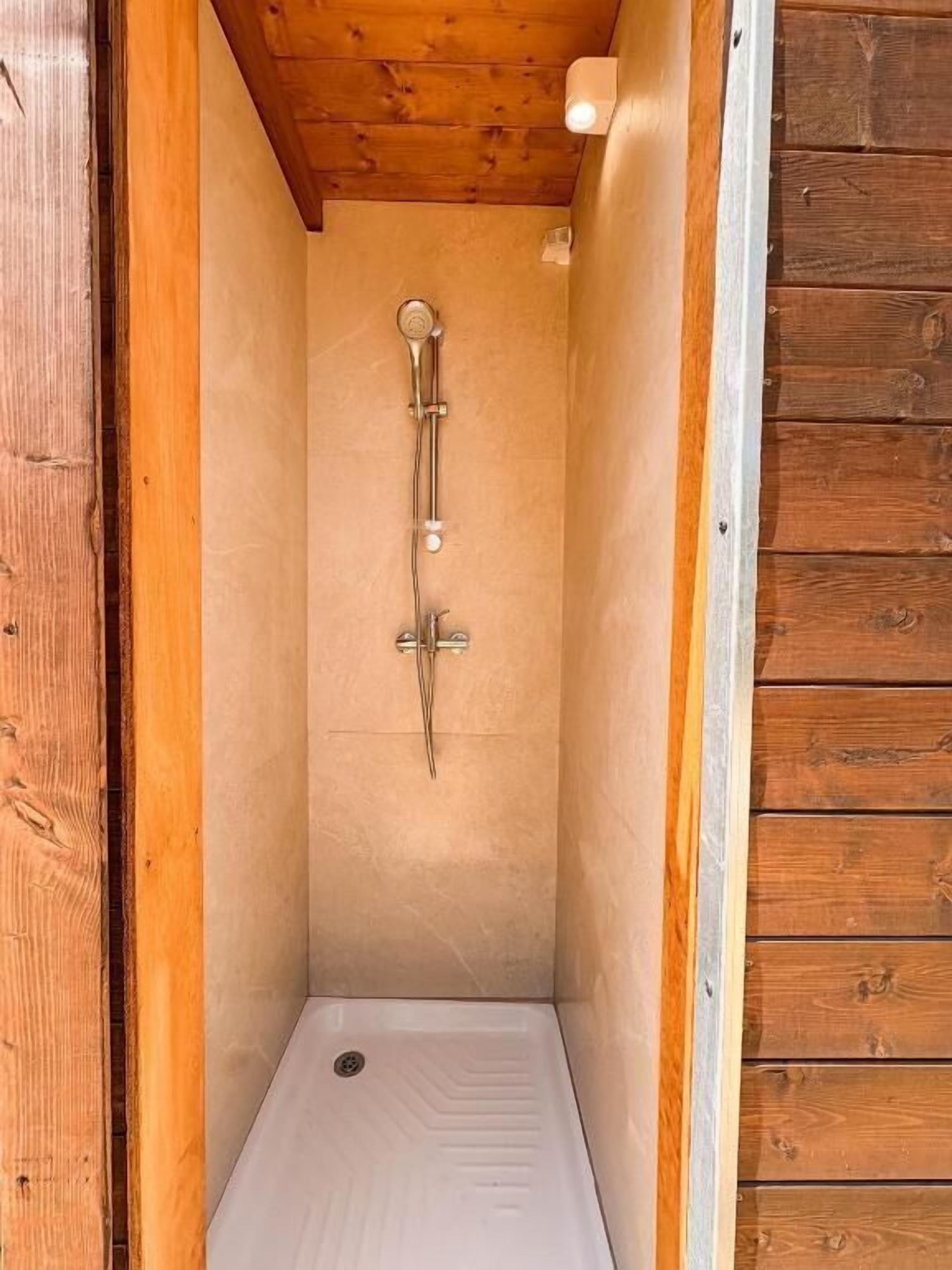 A small, enclosed shower area with a wooden ceiling and walls, a showerhead, and a drain.