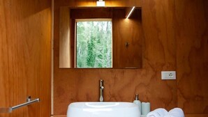 Une salle de bain en bois avec une grande fenêtre, un lavabo blanc et une serviette posée sur le comptoir.