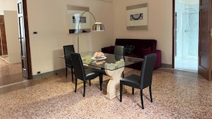A modern living room with a glass dining table, black chairs, a red sofa, and a ceiling-mounted TV. - Tintoretto Superior Apartment in historic Villa near Lucca (Matraia)