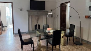 A dining area with a glass table, black chairs, a fireplace, and a television on the wall. - Tintoretto Superior Apartment in historic Villa near Lucca (Matraia)