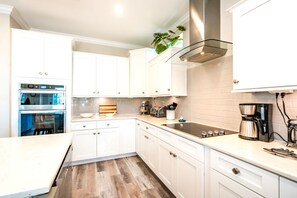 Une cuisine moderne avec des meubles blancs, des appareils électroménagers en acier inoxydable et un plancher en bois.