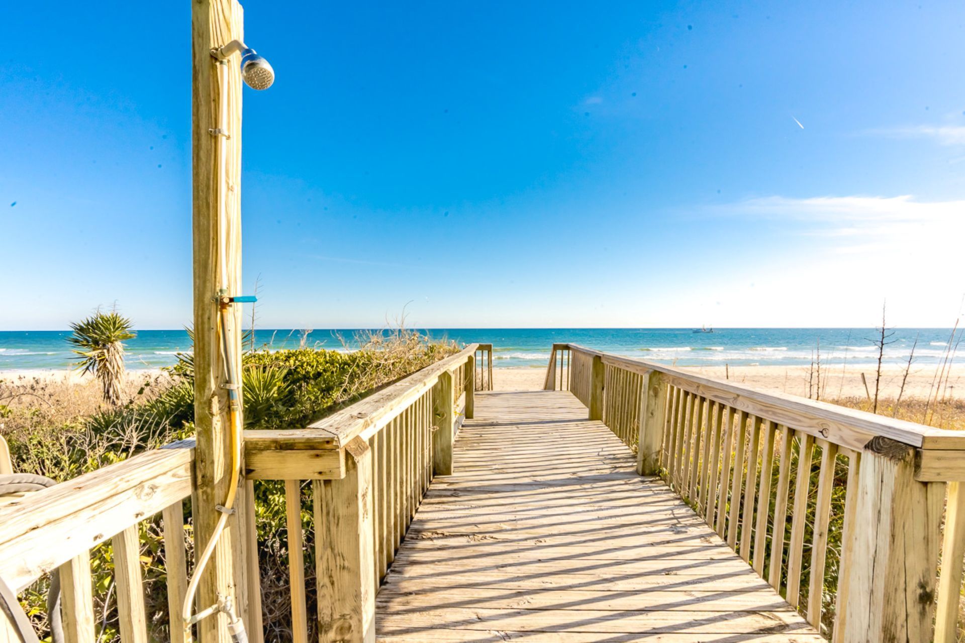 Una pasarela de madera que conduce a una playa con cielos despejados.