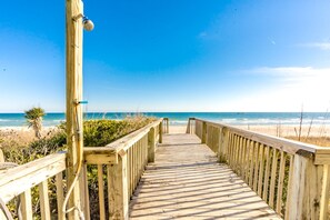 Une promenade en bois qui mène à une plage, avec un ciel dégagé.