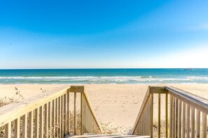 Ein hölzerner Steg führt zu einem Strand bei strahlendem Himmel.