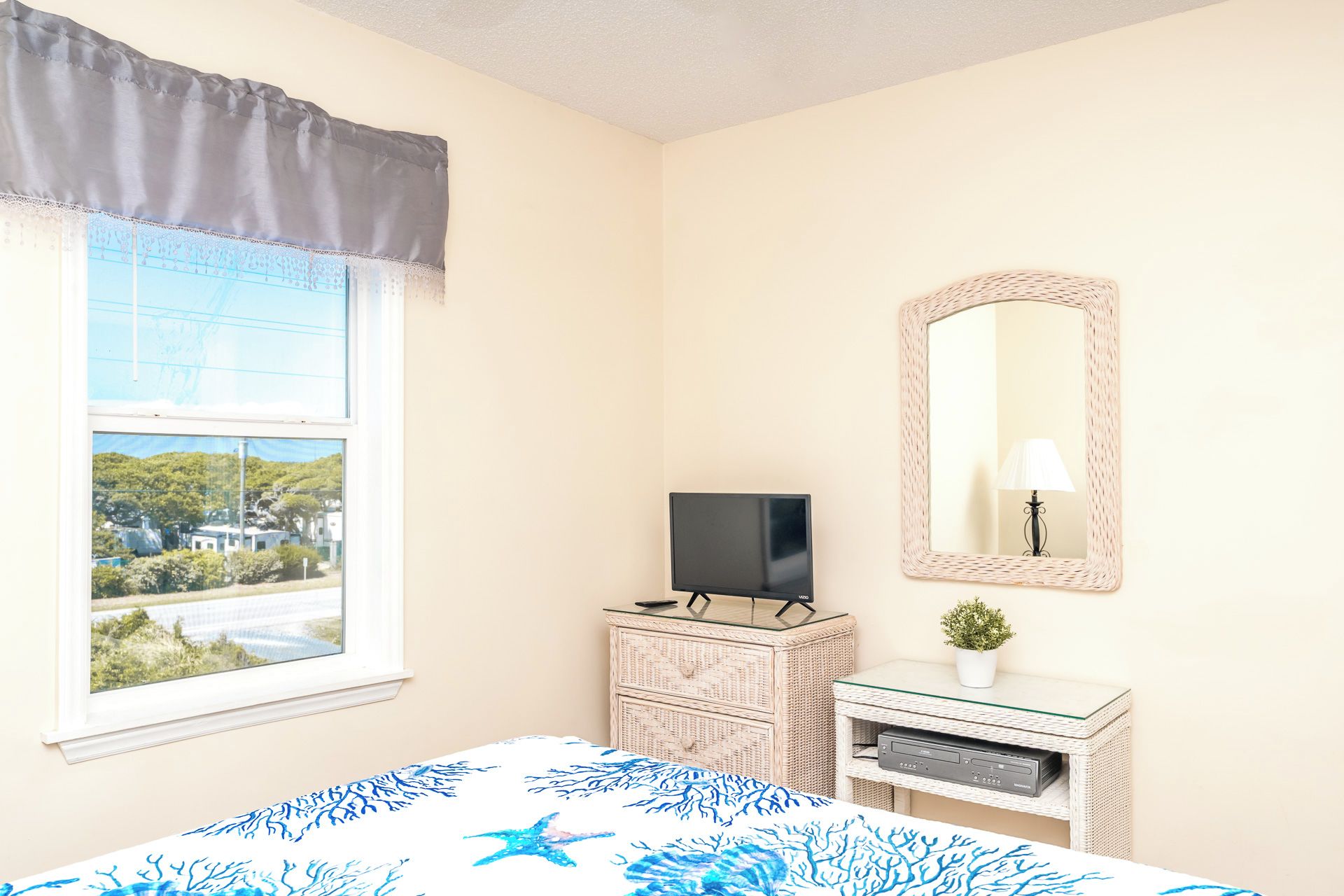 A bedroom with a bed, a dresser, a television, a mirror, and a window with a view of a landscape.