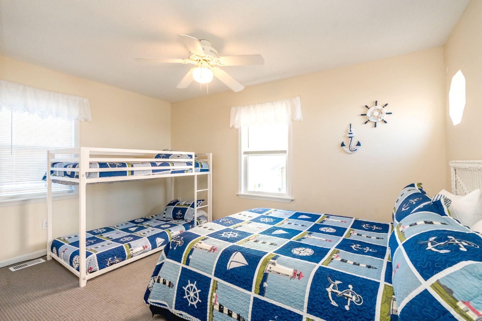 A bedroom with bunk beds, a ceiling fan, a window with curtains, and nautical-themed wall decorations.