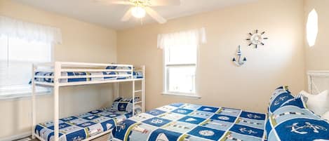 A bedroom with bunk beds, a ceiling fan, a window with curtains, and nautical-themed wall decorations.
