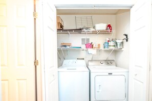 A laundry room with a washing machine, dryer, and shelves with various items. - A Porpoiseful Life - Oceanfront 4 BR Duplex, 2 Decks and Dog Friendly! (N. Topsail Beach)