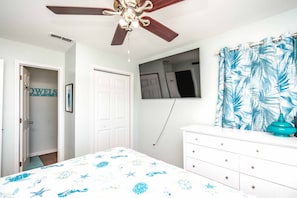 A bedroom with a bed, a dresser, a ceiling fan, a door, and a window with a curtain. - Castaway - 3 BR, Oceanfront Gem with 2 Sun Decks (Surf City)