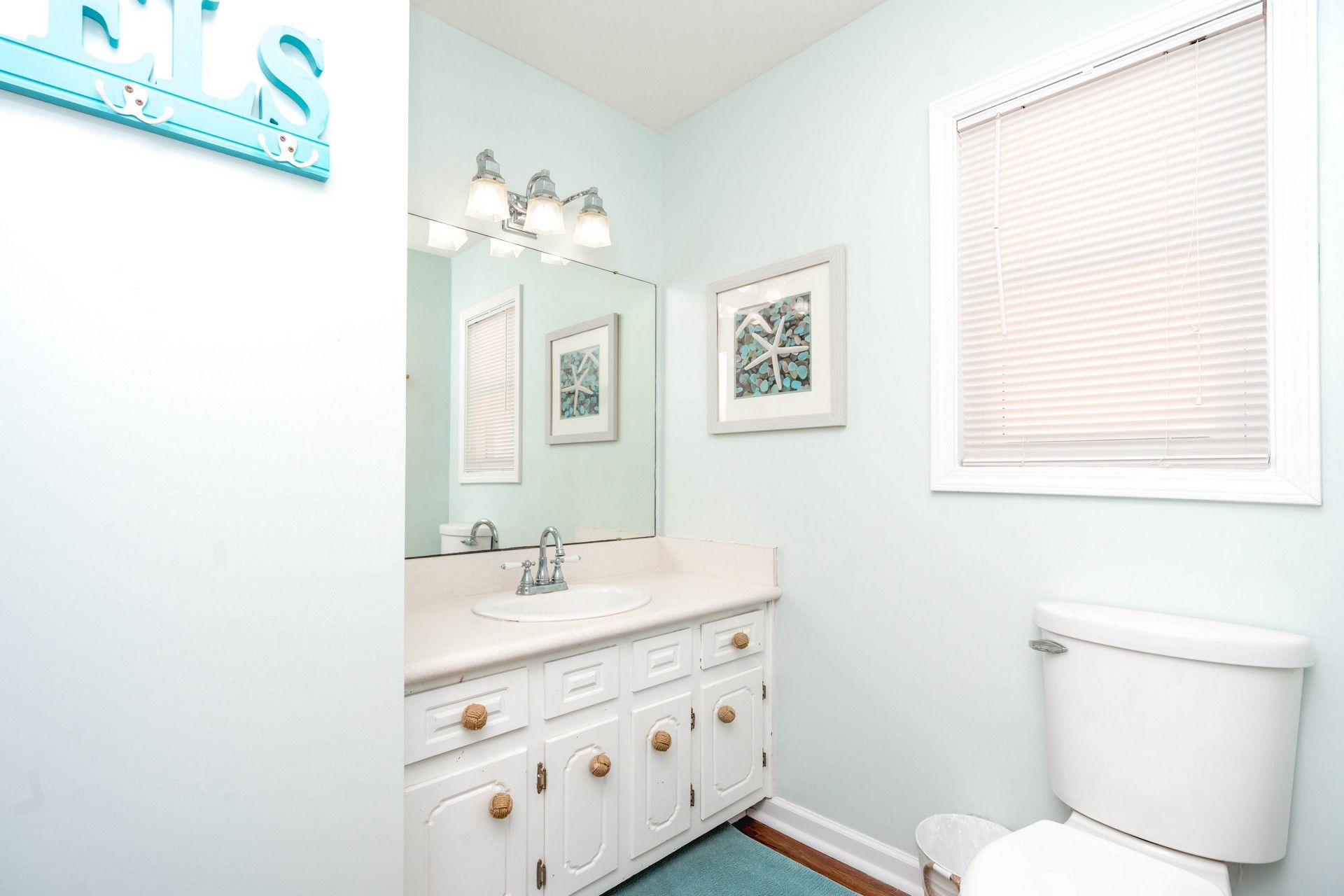 A bathroom with a white sink, a mirror, a toilet, and a window with blinds.