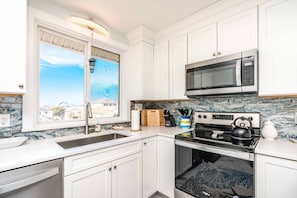 A modern kitchen with white cabinetry, a built-in microwave, a stove, and a sink. - Castaway - 3 BR, Oceanfront Gem with 2 Sun Decks (Surf City)