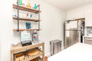 A kitchen with a stainless steel refrigerator, a coffee machine, and a shelf with decorative items. - Castaway - 3 BR, Oceanfront Gem with 2 Sun Decks (Surf City)