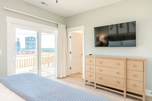 A bedroom with a bed, a dresser, a TV, and a sliding glass door leading to a balcony. - Current Situation - 4 BR Modern Townhouse In Great Location (Surf City)
