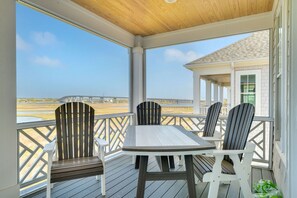 A covered outdoor seating area with a table and chairs, overlooking a body of water and a bridge. - Twin Shores - 6 BR, Heated Pool, Great Sound Views, Built in 2025 (Surf City)