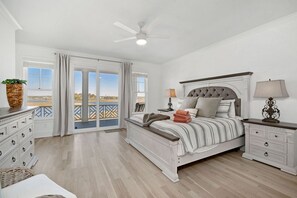 A bedroom with a bed, nightstands, a dresser, a ceiling fan, and a view through a glass door. - Twin Shores - 6 BR, Heated Pool, Great Sound Views, Built in 2025 (Surf City)