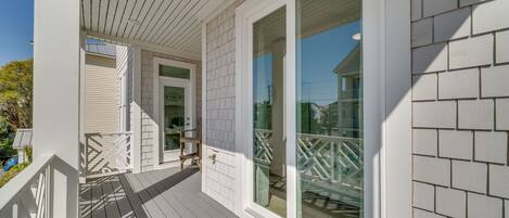 A covered porch with a white railing, a door, and large glass windows.