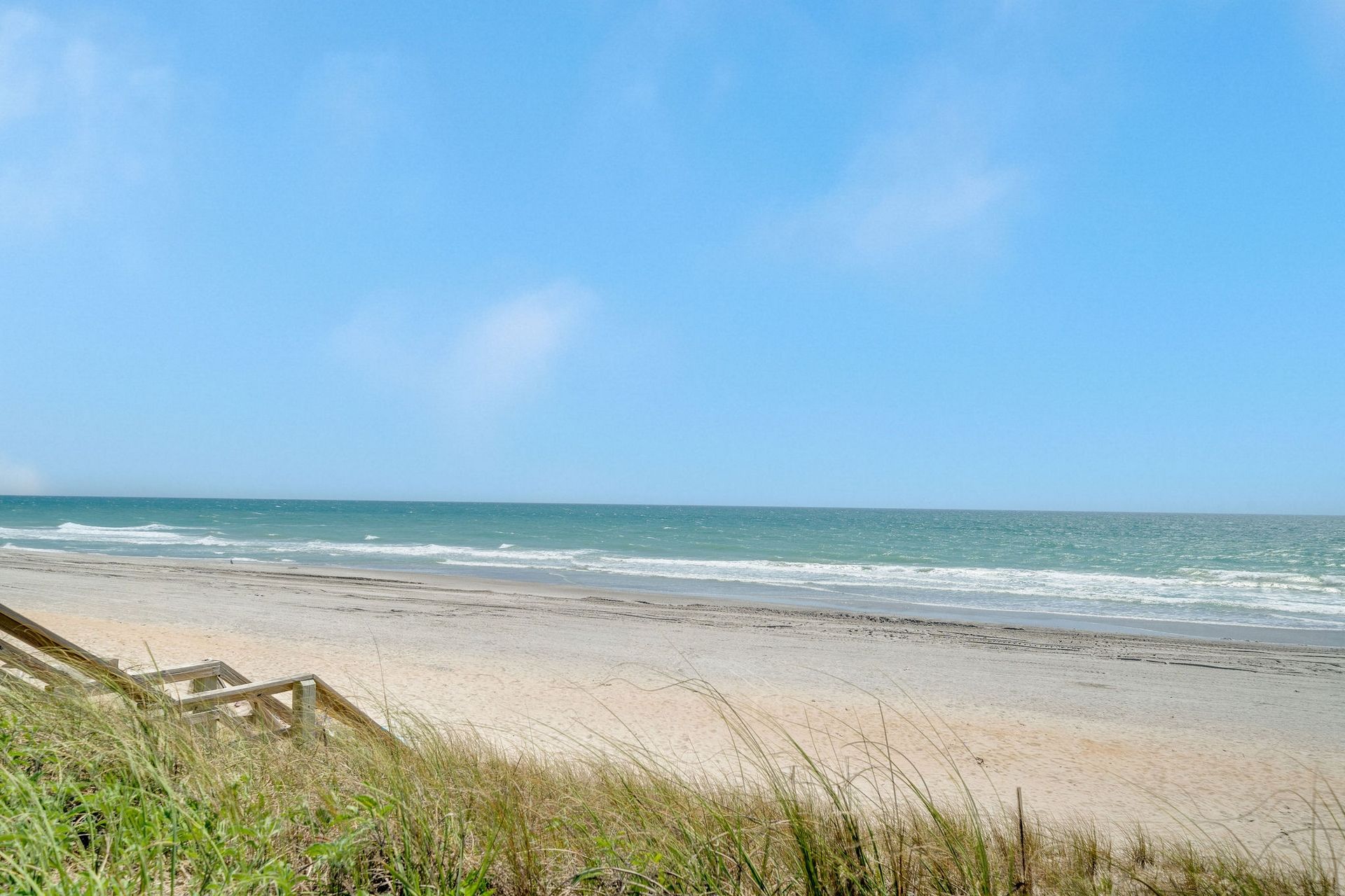 Une plage avec un ciel dégagé, un rivage sablonneux et une promenade en bois qui mène à l’eau.