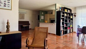 Un salon spacieux avec un fauteuil en osier, une bibliothèque et un coin repas comprenant une table et des chaises.