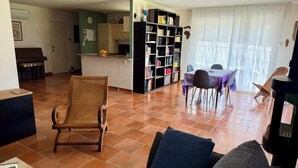 Un salon comprenant un canapé, un fauteuil, une bibliothèque et un coin repas avec une table et des chaises.