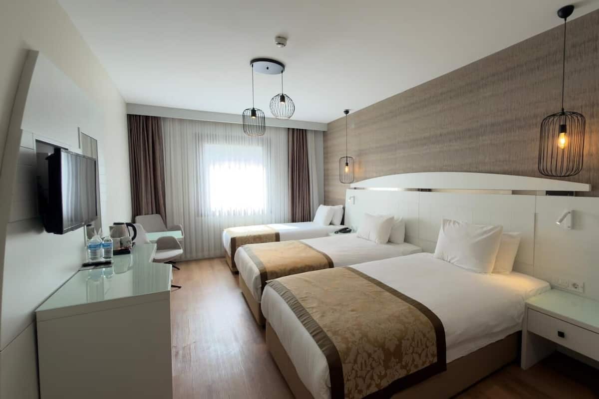 Quarto de hotel com duas camas, televisão, escrivaninha e luminária moderna.