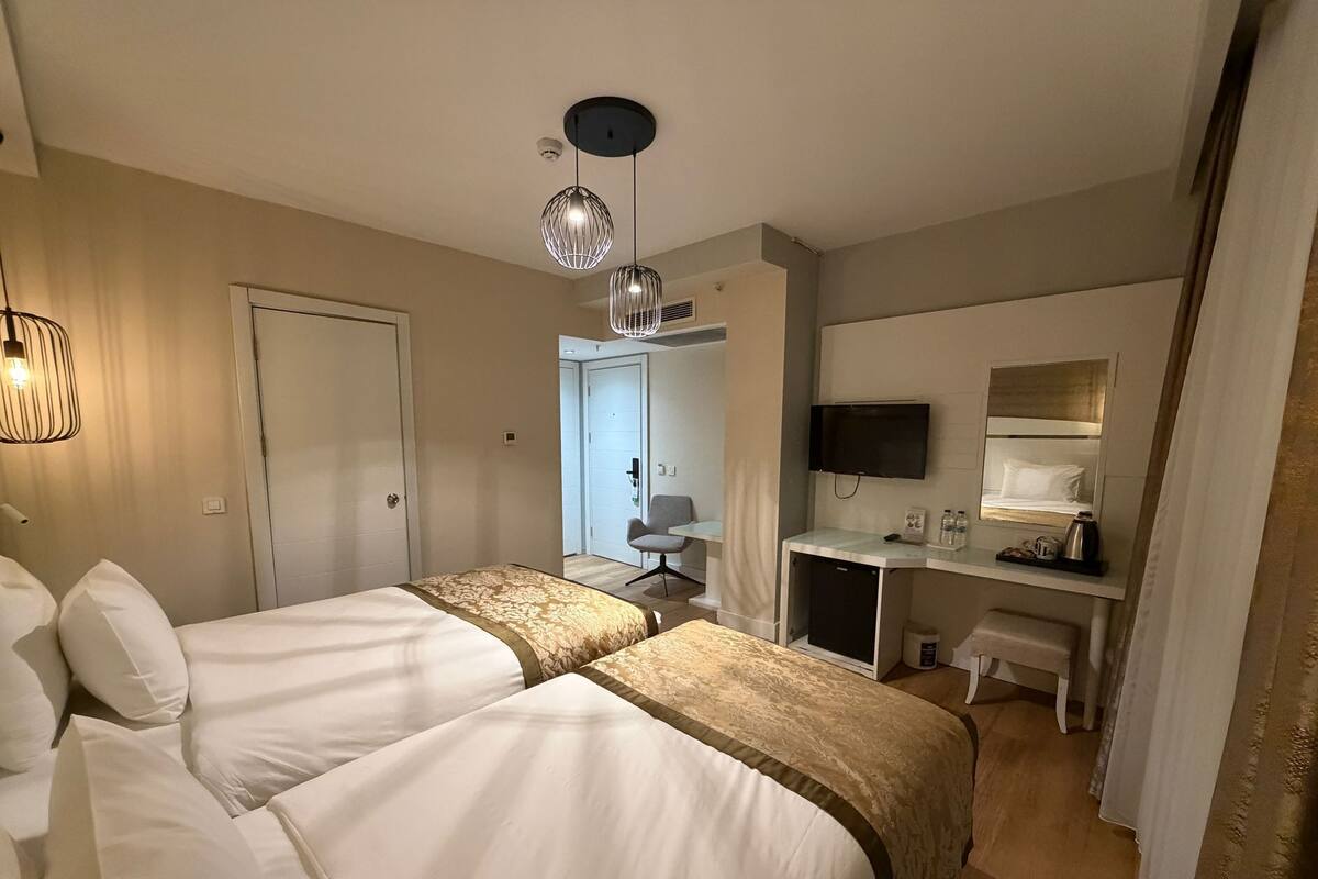 Quarto de hotel com duas camas, uma mesa com televisão, uma cadeira, uma pequena cozinha e uma porta que dá para outro quarto.